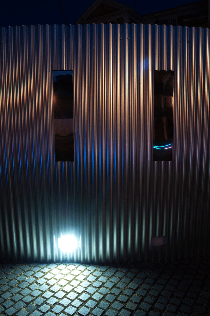 Anta Germane large scale public architectural artwork Interactive Tunnel showing colour effects at night on corrugated sheet and mirrored windows. Constructed from corrugated steel sheets, timber, one way persepx mirrors, PIR sensors and lights, situated in London Rootstein Hopkins Parade Ground.